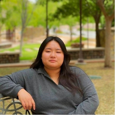 Tenzin Lhaden poses for a portrait on a bench in a park.