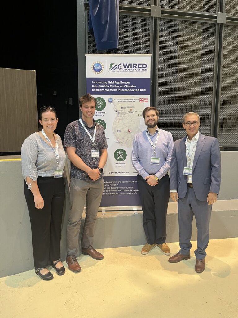 Kyle Goodrick, Masood Parvania, and two others posing in front of the WIRED  Grid Resilience Symposium sign.